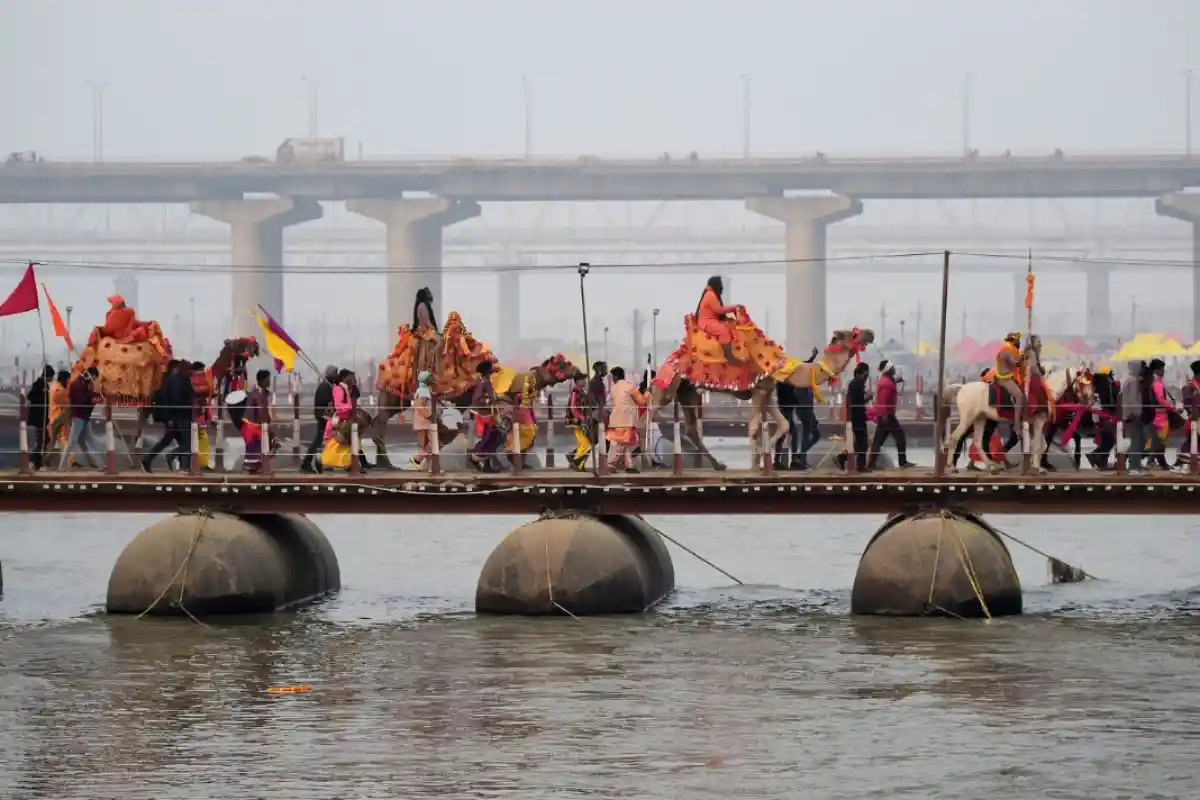 Close-up of Naga sadhus entering the river during Shahi Snan; saffron flags; trishuls; conches; large crowds; high-detail documentary style.